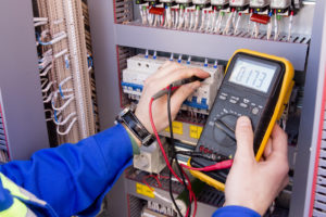 multimeter is in hands of engineer in electrical cabinet. Adjustment of automated control system for industrial equipment control cabinets. electrician measures voltage by tester. an electrician measuring voltage with a multimeter